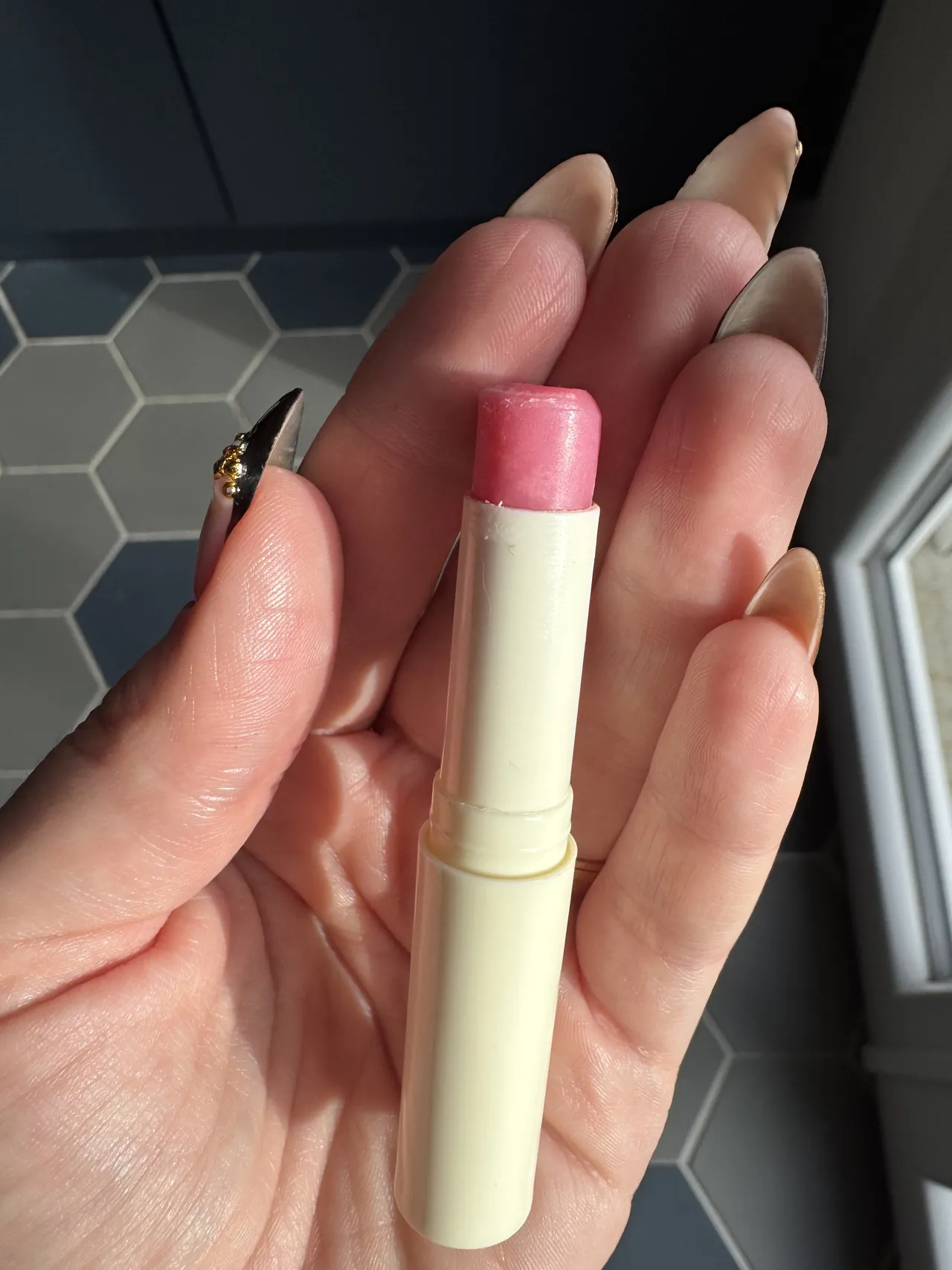 Un stick de baume à lèvres teinté rose, tenu dans la main